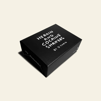 A black box on a light background shows SHRIG SHOP HEROIN AND COCAINE PORCELAIN SHAKERS in white hand-drawn letters—quirky salt and pepper shakers from Shrig Shop for fans of unique collectibles.