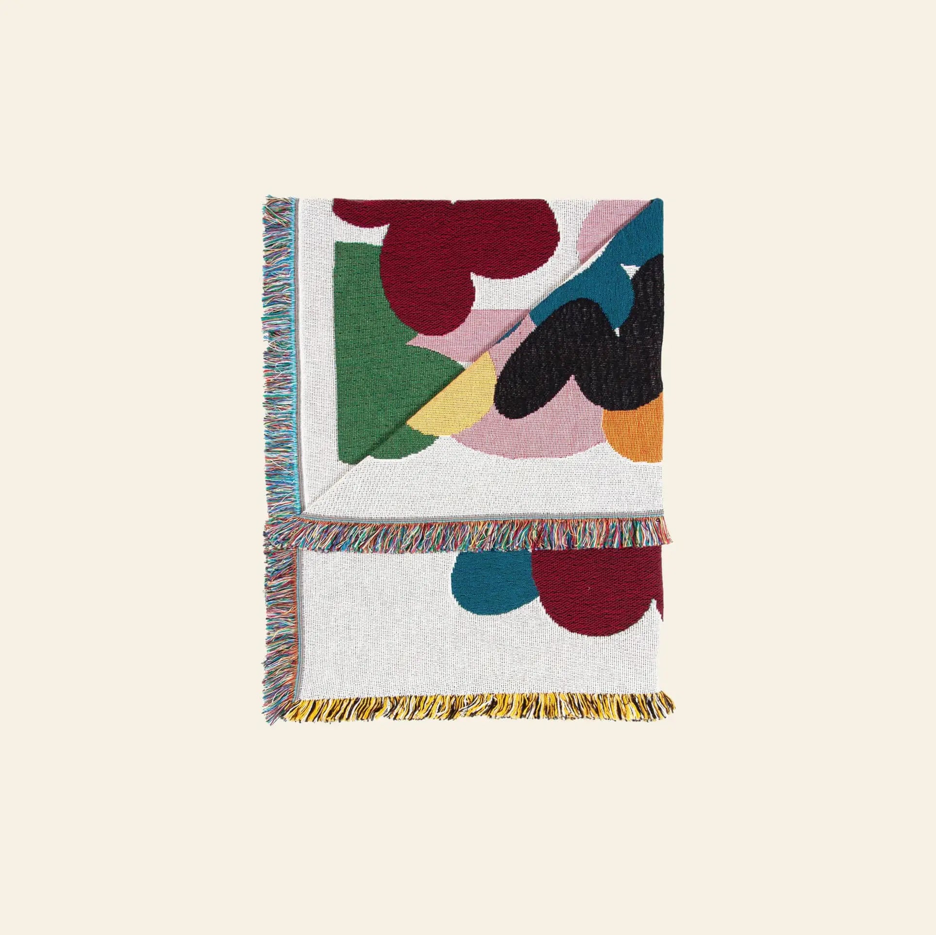 The Slowdown Studio Alessi Throw is a folded, recycled cotton blanket with colorful abstract shapes and multicolored fringe, shown on a light neutral background—a sustainable choice from Slowdown Studio.