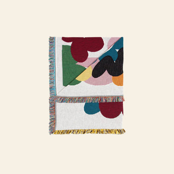 The Slowdown Studio Alessi Throw is a folded, recycled cotton blanket with colorful abstract shapes and multicolored fringe, shown on a light neutral background—a sustainable choice from Slowdown Studio.