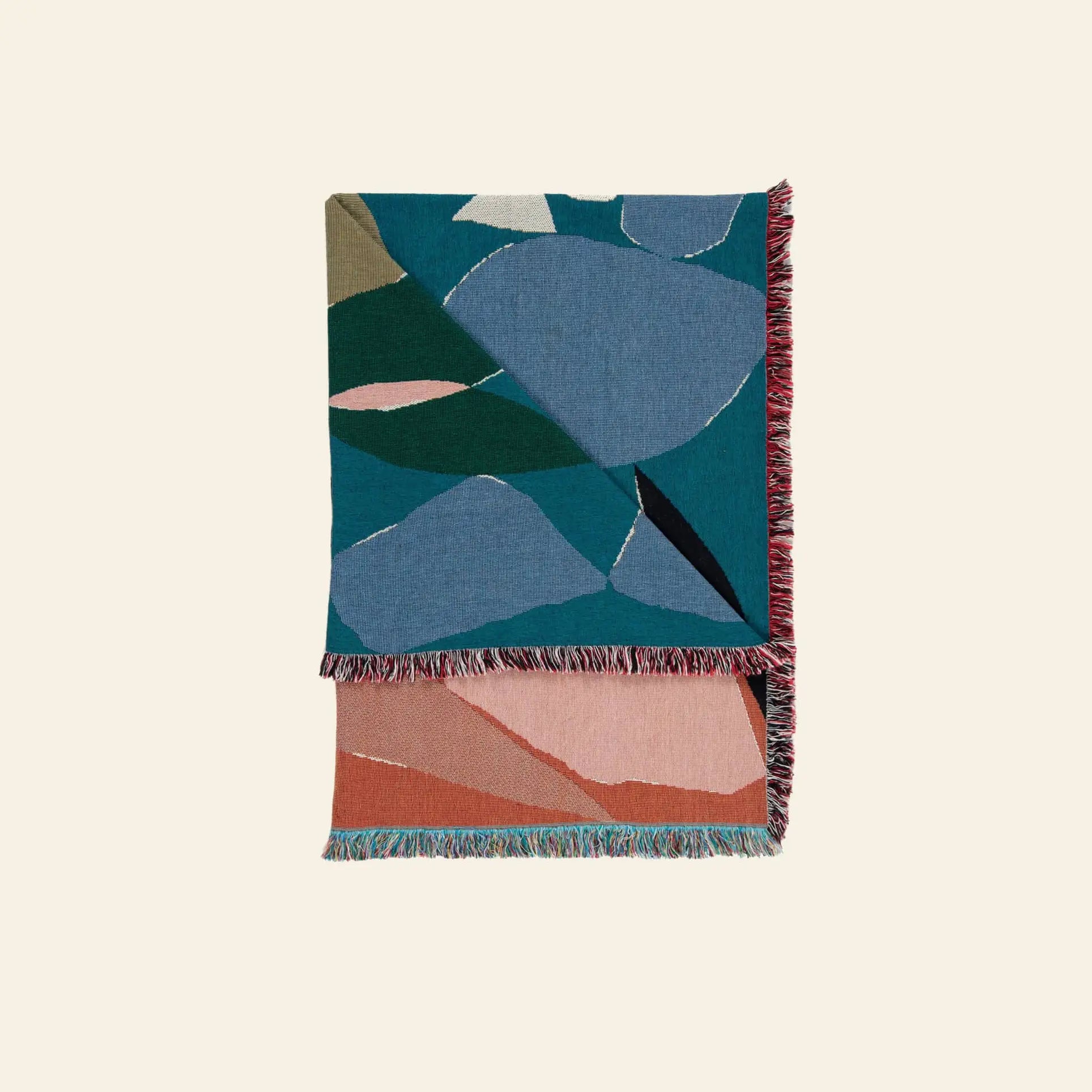 The Slowdown Studio Barbosa Throw features abstract geometric patterns in blue, green, and gray on top, peach, pink, and terracotta underneath, and has multicolored fringed edges. Crafted from recycled cotton by Slowdown Studio.