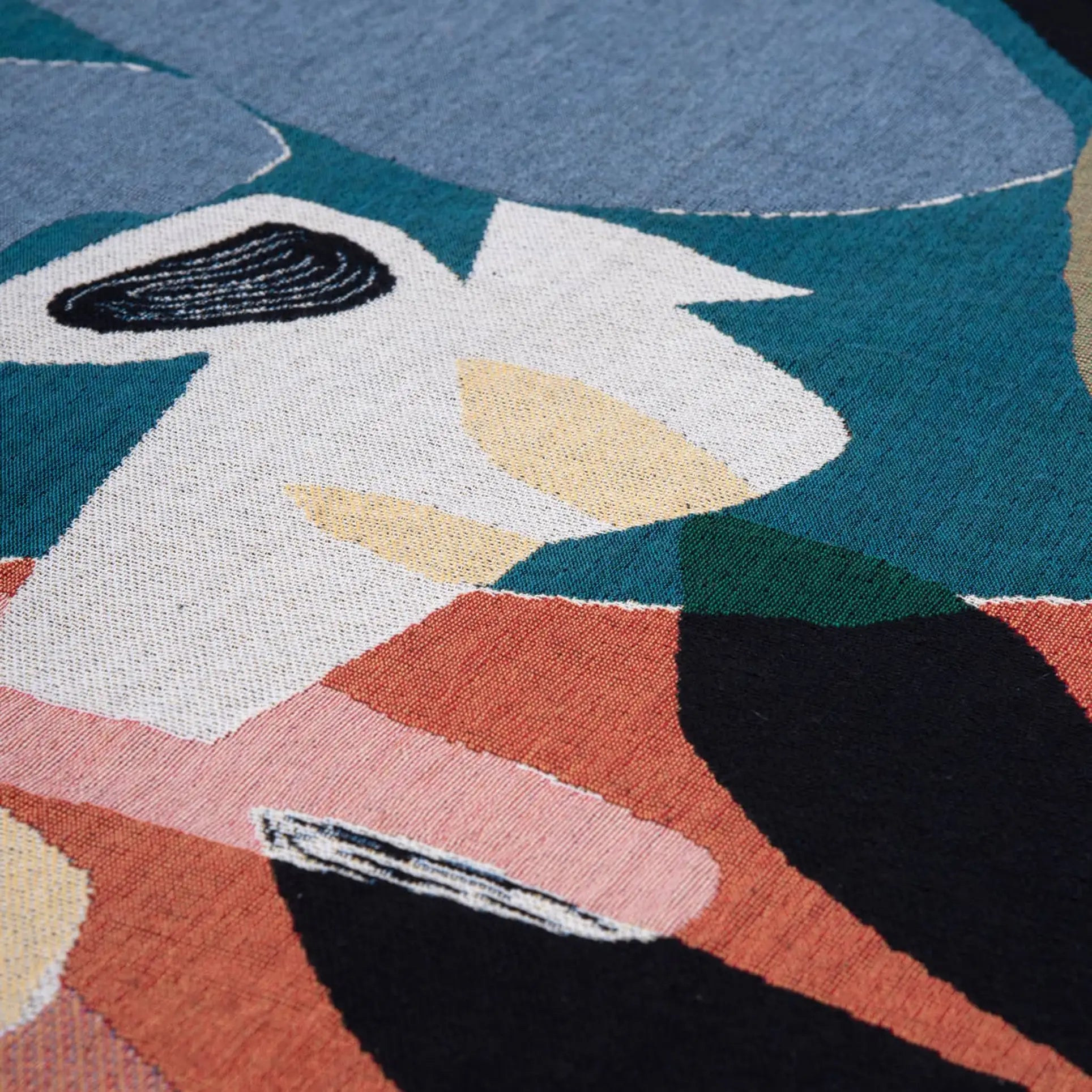 Close-up of the Slowdown Studio Barbosa Throw, an abstract, woven textile crafted from recycled cotton with overlapping shapes in blue, teal, cream, pink, black, and mustard yellow for a modern artistic look.