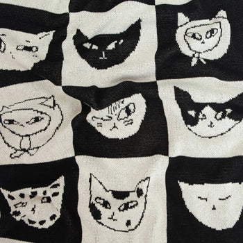 The Slowdown Studio Cat Bingo Mini Blanket features a black and white grid of cartoon cat faces with different expressions, crafted from a soft recycled cotton blend by Slowdown Studio.