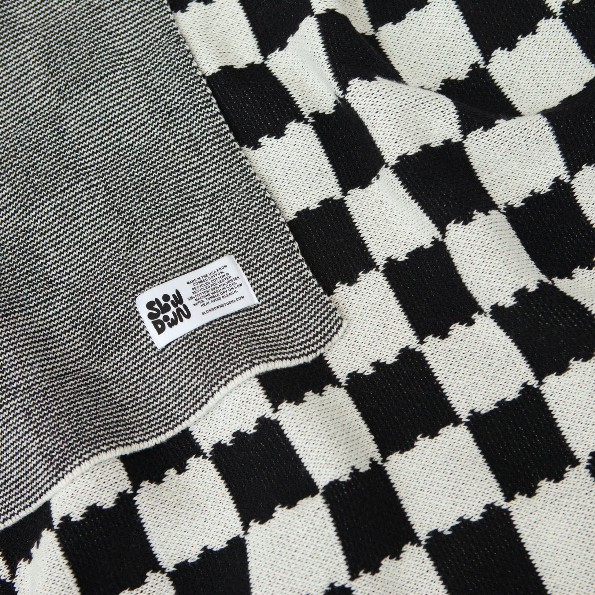 A close-up of the Slowdown Studio Chilton Black/White Knit Blanket, made from recycled cotton with a checkered pattern and a sewn-on Slowdown Studio label.