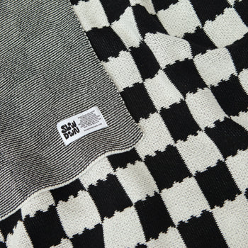 A close-up of the Slowdown Studio Chilton Black/White Knit Blanket, made from recycled cotton with a checkered pattern and a sewn-on Slowdown Studio label.
