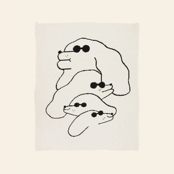 The Slowdown Studio Dawgs Mini Blanket features a minimalist illustration of three stacked dogs in sunglasses, drawn in black lines on white, inspired by Slowdown Studio. Made from recycled cotton.
