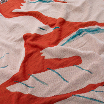 A close-up of the Slowdown Studio Passaro Throw by Slowdown Studio, crafted from recycled cotton with an abstract red, teal, and off-white pattern. The eco-friendly fabric features bold, irregular lines and shapes with a soft, textured finish.