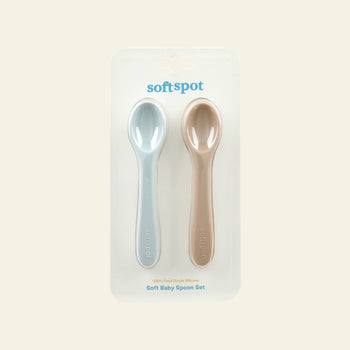 Soft Spot Soft Baby Spoons, Set of 2, are gently displayed side by side in clear packaging. Perfect as babys first spoons, these silicone utensils from Soft Spot soothe teething gums and make feeding easy against a light cream background.