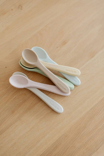 Two sets of Soft Spot Soft Baby Spoons, each in pastel shades, are stacked on a light wooden surface. Gentle on teething gums and perfect for first feedings, these spoons feature “softspot” printed on the handles.