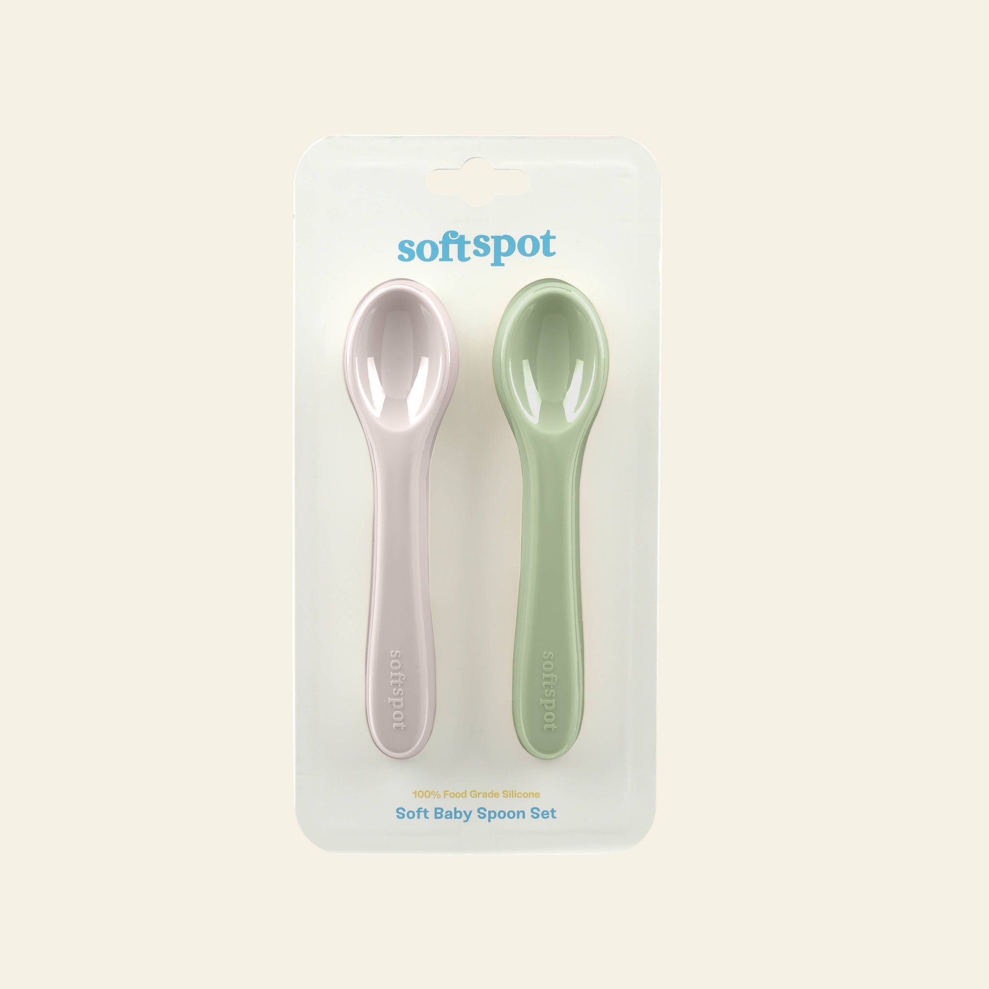 The Soft Spot Soft Baby Spoons, Set of 2, from Soft Spot includes pink and green silicone spoons for teething and easy feeding, packaged side by side in a clear blister pack against a light neutral background.