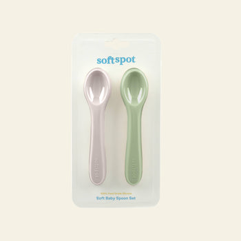 The Soft Spot Soft Baby Spoons, Set of 2, from Soft Spot includes pink and green silicone spoons for teething and easy feeding, packaged side by side in a clear blister pack against a light neutral background.