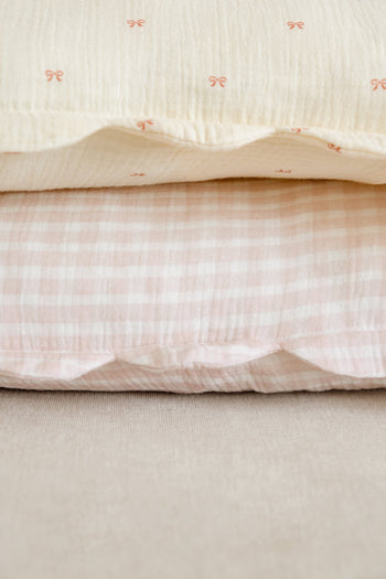 The Soft Spot Soft Petal Cushion Covers, Set of 2 by Soft Spot, includes a cream cover with red bows and a pink-and-white gingham check, both crafted from organic cotton for extra comfort.