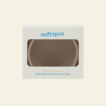 A beige food-grade silicone Soft Spot Soft Suction Bowl with a suction grip is displayed in white packaging with a transparent window. The box shows the Soft Spot logo and product name in blue and gold text.