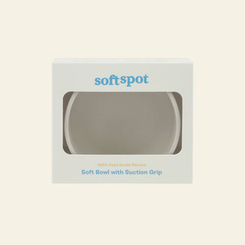 A white Soft Spot Soft Suction Bowl is packaged in a box with a clear window. The box displays Soft Spot on top and features Soft Bowls with Suction Grip and 100% food-grade silicone in blue and yellow text.