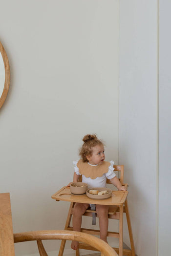 A young child with curly hair smiles in a wooden high chair, using Soft Spot’s Soft Suction Plate—designed for secure mealtimes with strong suction grip and a minimal, food-grade silicone look.