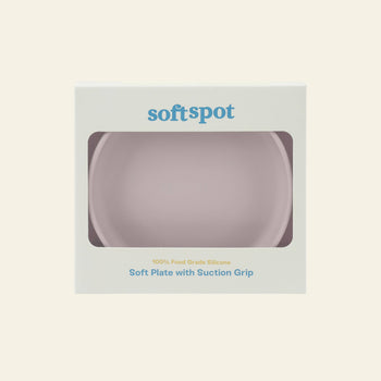 A boxed Soft Spot Soft Suction Plate by Soft Spot, made of food-grade silicone with a strong suction grip, visible through a front clear window. The light-colored box features blue and gray text for safe and fun mealtimes.
