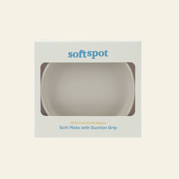 The Soft Spot Soft Suction Plate by Soft Spot is a white, food-grade silicone plate in softspot packaging. The box has a cut-out window showing the plate inside and highlights its strong suction for secure, mess-free meals.