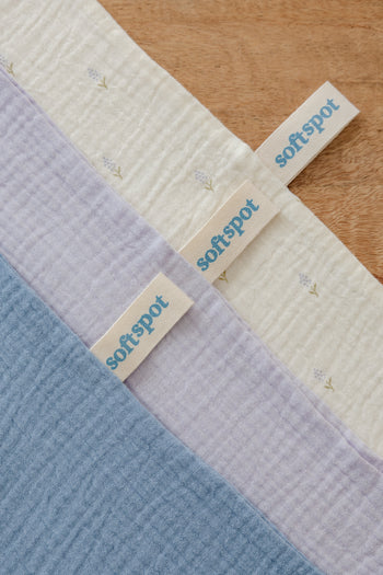 A neatly folded set of Soft Spot Soft Tea Towels (Set of 3) in cream and light blue, tied with a cream ribbon featuring the Soft Spot brand, sits against a plain light background—ideal as placemats or tea towels.