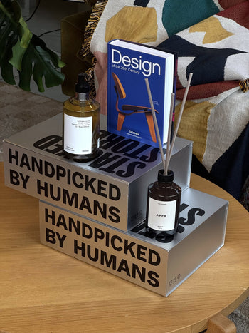 The Stacked Store The Design Enthusiast Gift Box features two gray boxes labeled "HANDPICKED BY HUMANS," an APFR Reed Diffuser, a dropper bottle, and the book Design of the 20th Century—ideal for any design lover.