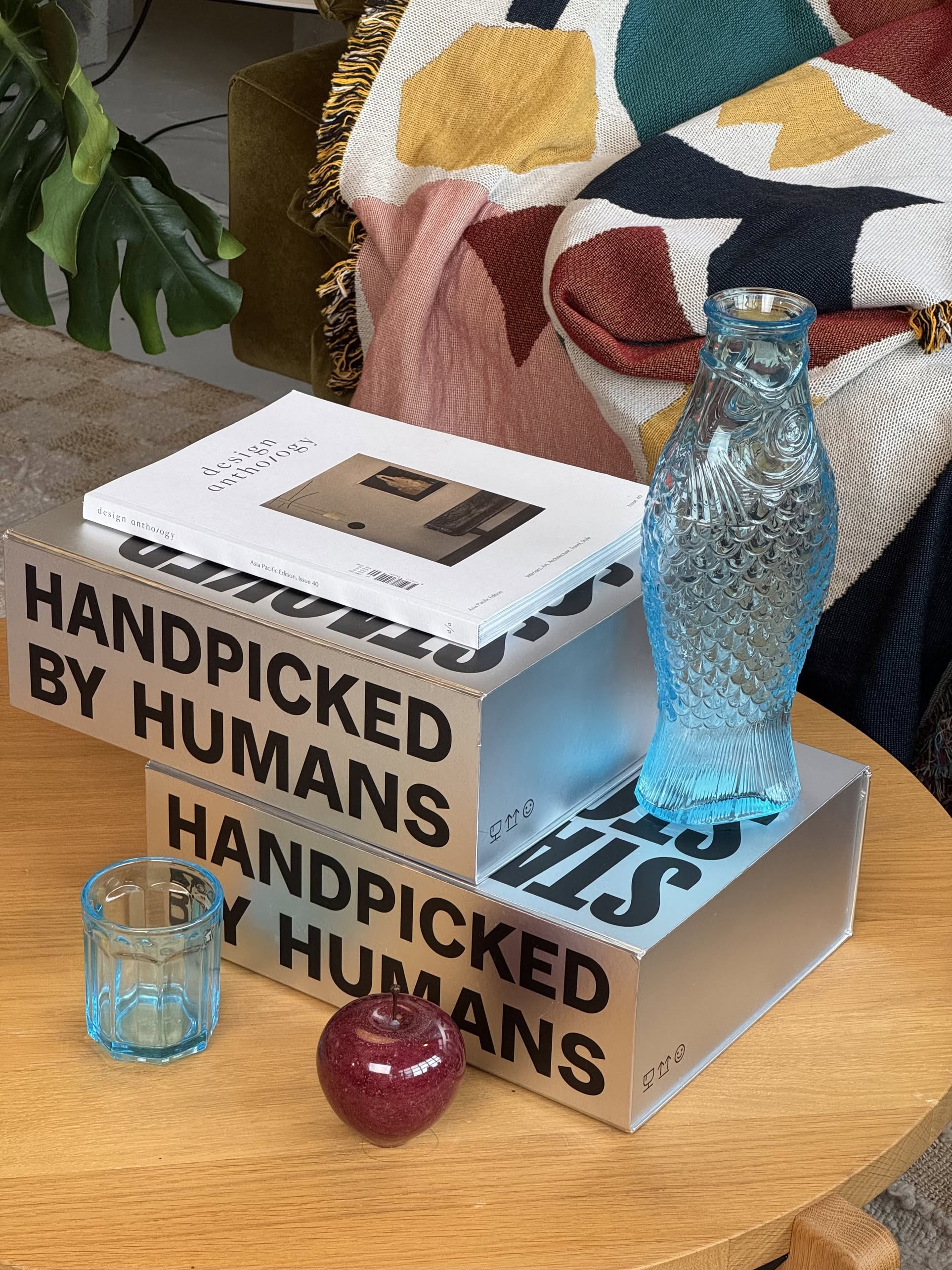 The Stacked Store The Minimalists Gift Box by Stacked Store sits on a wooden table alongside colorful glassware and books, with a vibrant blanket draped over a chair—creating the perfect design-forward gift scene.