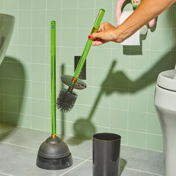 A hand grabs the Staff The Toilet Brush - Green by Staff from its holder next to a matching plunger in a tiled bathroom, with a toilet and toilet paper roll visible in the background.