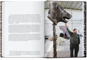 A man in a spacious studio reaches up to touch a large bronze animal head sculpture by Ai Weiwei, as featured in the TASCHEN Ai Weiwei monograph. The opposite page shows multilingual text blocks.
