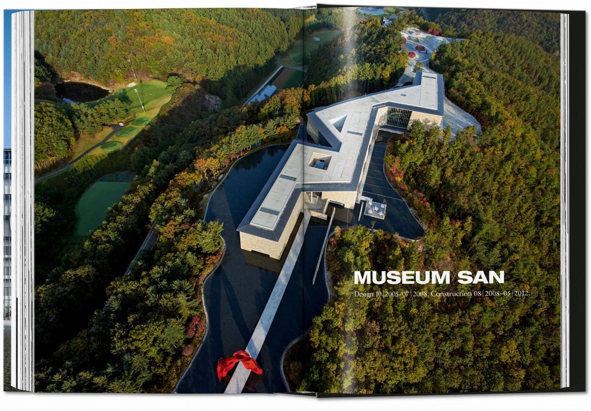 An aerial photo of Museum SAN by Tadao Ando appears across two pages in "TASCHEN Ando: Complete Works 1975-Today" by TASCHEN, showing its angular minimalist design amid lush forest and water, with the title MUSEUM SAN on the image.