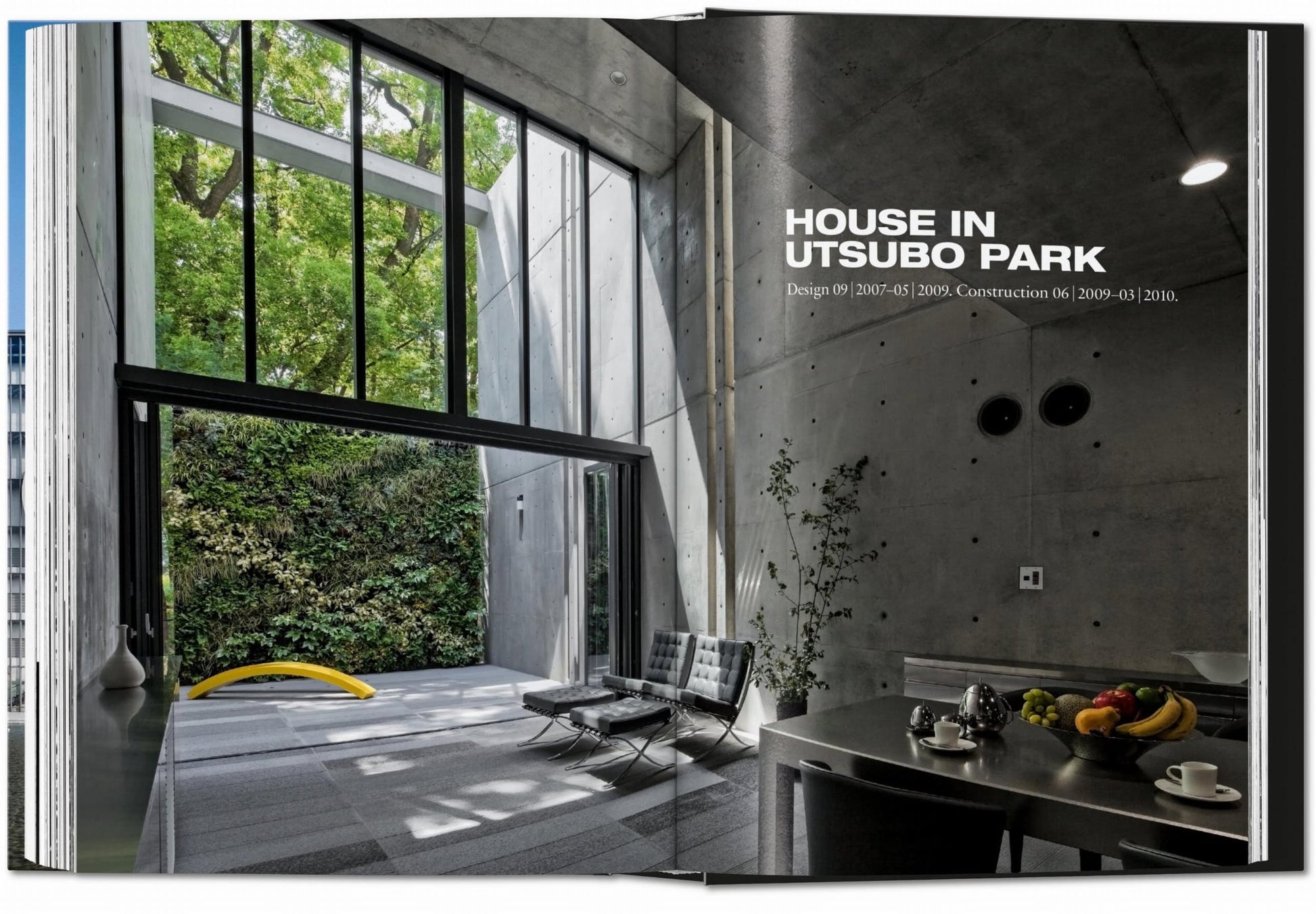 A minimalist living space inspired by Tadao Ando, featuring high concrete walls, large windows, a garden patio, and TASCHEN’s “Ando: Complete Works 1975-Today” book by TASCHEN on display. Black chairs and a yellow curved bench add modern touches.