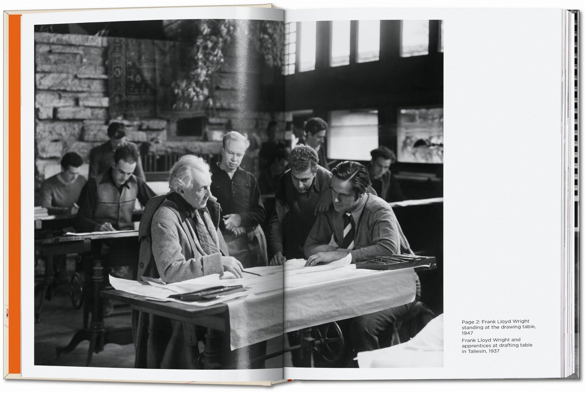 Black and white photo from TASCHEN Frank Lloyd Wright shows Frank Lloyd Wright at a drafting table with apprentices, reviewing plans in a studio, circa 1951. Several men are gathered around the table in discussion. Brand: TASCHEN.