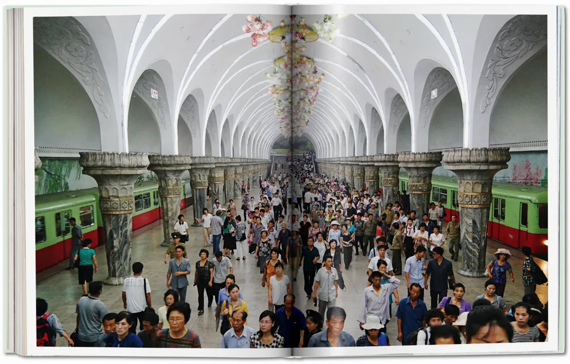 TASCHEN Inside North Korea captures crowds moving through ornate subway stations with white vaulted ceilings, decorative columns, murals, and green and red trains lining bustling platforms.