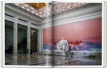 A grand marble hall, reminiscent of Oliver Wainwright’s imagery in TASCHEN Inside North Korea, features tall columns, a white statue before a pink mountain mural, two admirers, and an escalator from TASCHEN.