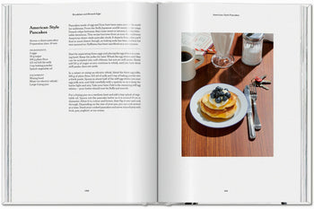 The TASCHEN The Gourmand’s Egg cookbook lies open on a rustic wooden table, with an egg pancake recipe and a vibrant photo of pancakes topped with blueberries, syrup, and coffee—blending food artistry from TASCHEN.