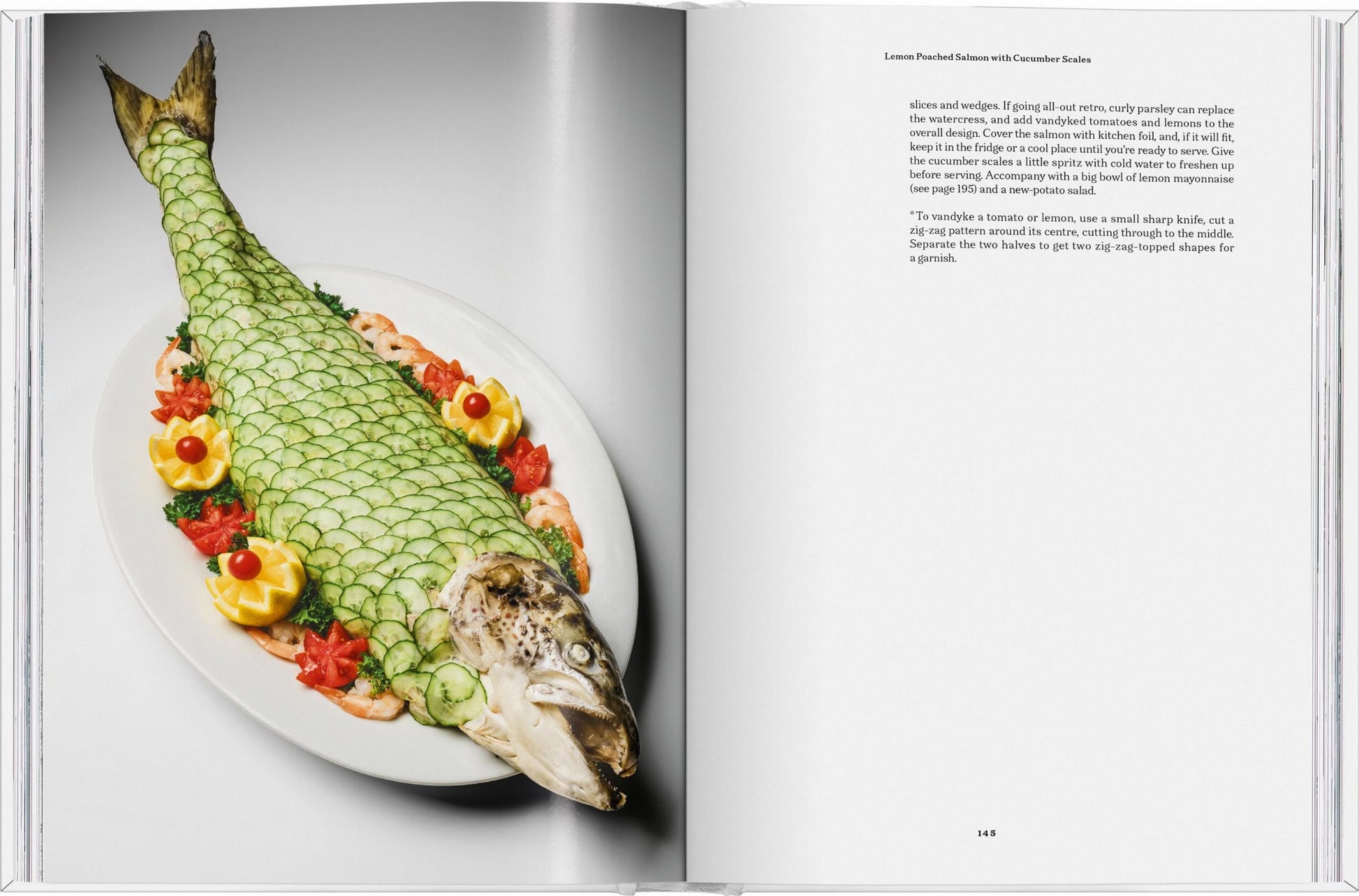 On the left page of TASCHEN The Gourmands Lemon: A Collection of Stories and Recipes, a whole salmon is artfully plated with cucumber scales, lemon slices, shrimp, and tomato flowers on a white oval dish.