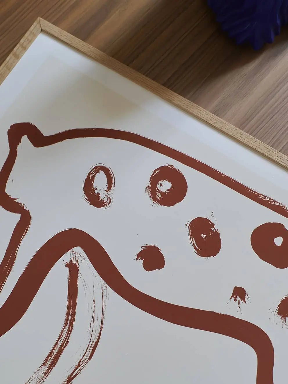 The Poster Club Anna Mörner - Statue (50x70) is a framed abstract fine art giclée print by The Poster Club, featuring a minimalist brown line animal with spots on premium art paper, displayed on a wooden surface.