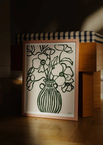 The Poster Club Anna Johansson - Monday (30x40) art print, featuring floral line drawings, leans against a wooden bench with a checkered cushion, bathed in warm sunlight on a wooden floor. Brand: The Poster Club.