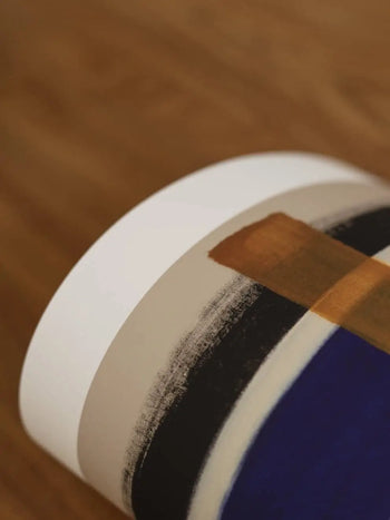 A close-up of The Poster Club Berit Mogensen Lopez - Checkered (50x70), showing bold brown, black, beige, and deep blue bands on white, set on wood—an elegant art print from The Poster Club.