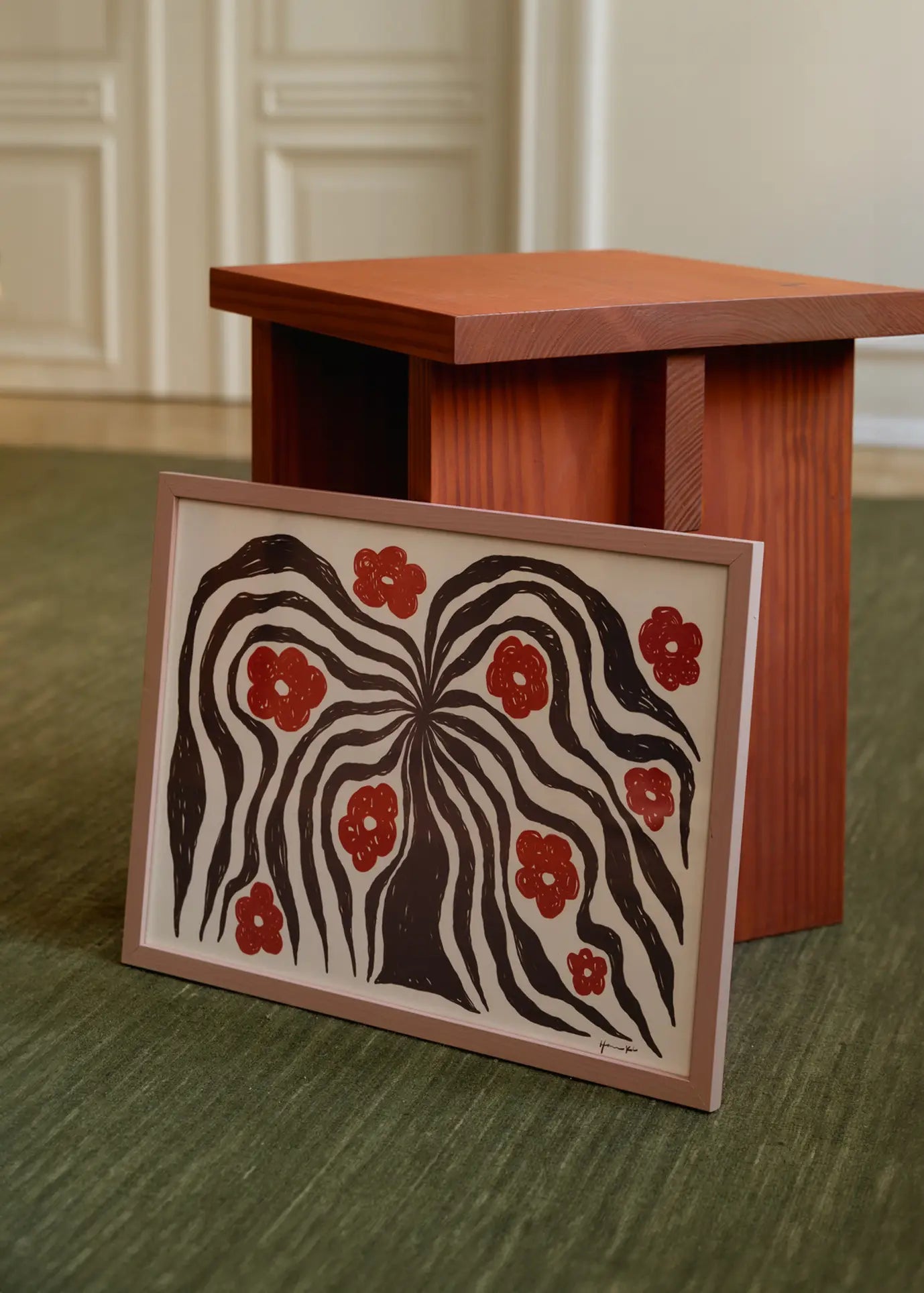 The Poster Club Hanna KL - Flux (30x40) art print, showing wavy black lines and red floral shapes, leans on a small wooden table atop a green carpet, with white paneled doors in the background.