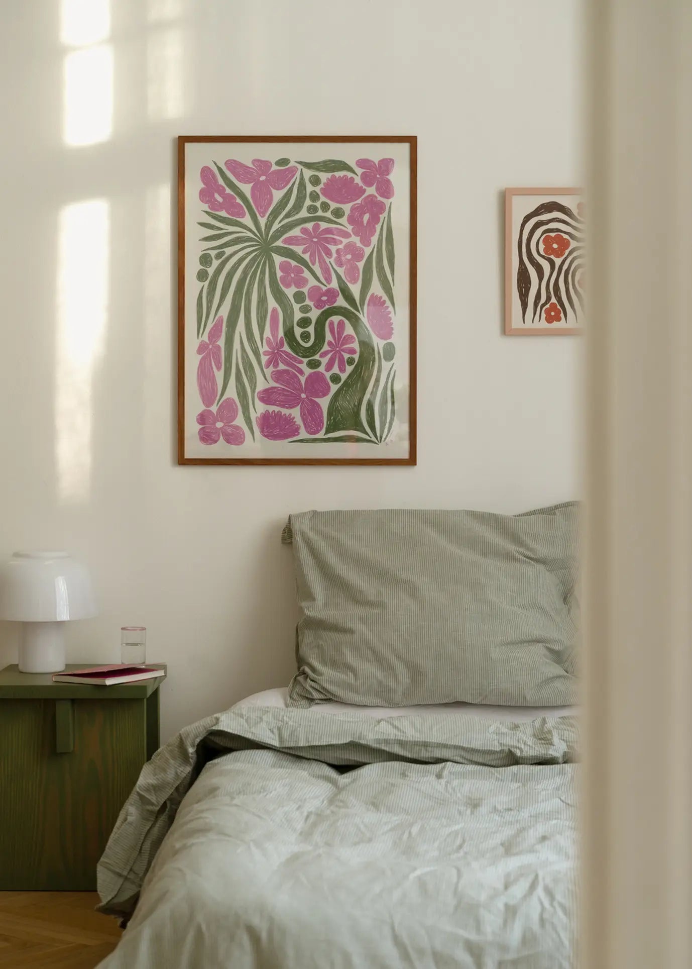 A cozy bedroom features a neatly made bed with green-striped bedding, a green nightstand with a white lamp and glass of water, and The Poster Club Hanna KL - Wonder (30x40) art print adding colorful floral charm above the bed.