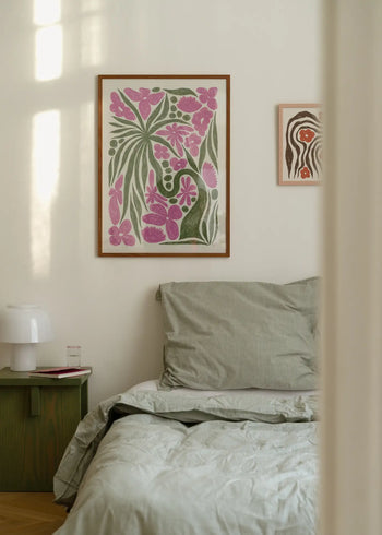 A cozy bedroom with a neatly made bed in light gray bedding, a green nightstand, and The Poster Clubs Hanna KL - Wonder (50x70) art print displayed above the bed amid colorful floral and abstract designs on the white wall.