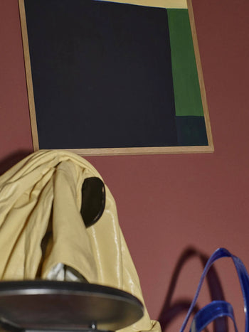 The Poster Club’s Hanna Peterson - Court (30x40) features dark, blue, green, and ivory blocks on red. Below, a shiny yellow jacket drapes over a chair beside part of a blue bag.