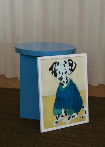 The Poster Club’s Hanna Peterson - Dalmatian In Sweatshirt (50x70) art print features a Dalmatian in a blue sweater beside a round blue table, set against beige curtains and a brown carpet.