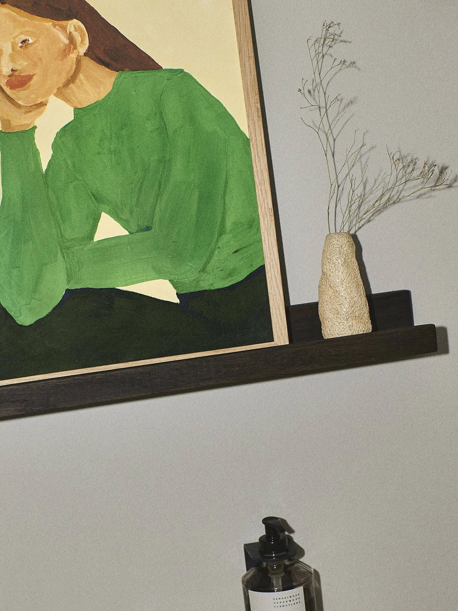 The Poster Club’s framed fine art giclée print, Hanna Peterson - Green Guise (30x40), features a person in a green shirt on a dark shelf beside a beige vase with dried flowers and a dark pump bottle below.
