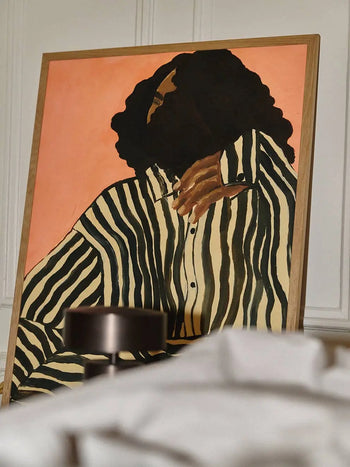 The Poster Clubs Jaguar 01 (50x70) by Anastasia Krasilnikova features a person with dark, curly hair in a black-and-white striped shirt on a warm peach background, framed and propped against a wall.