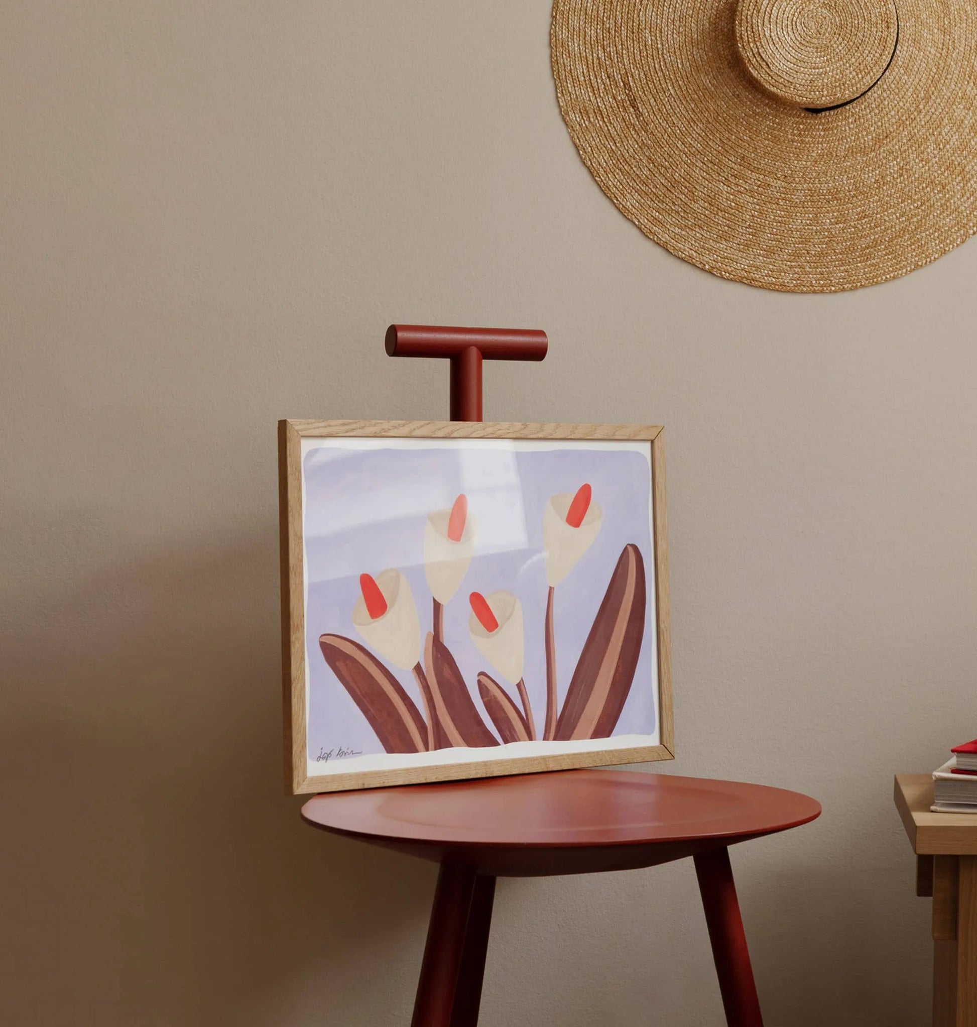 The Iga Kosicka - Flowers 03 (30x40) art print from The Poster Club sits on a red chair by a beige wall, with a straw hat hanging nearby and part of a wooden desk in view.