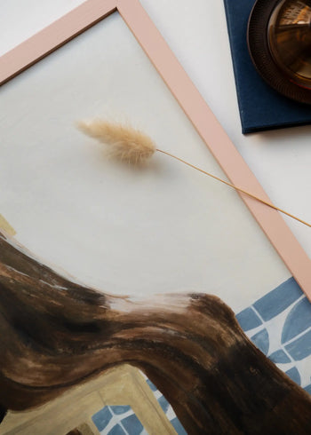 A close-up of The Poster Club’s Isabelle Vandeplassche - Chair With Blanket (70x100) art print shows soft pink edges, a figure with long brown hair, blue tile details, and nearby dried grass with a brown glass object.