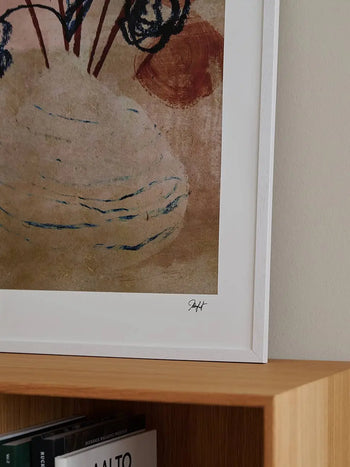 A corner of The Poster Club Madelen Möllard - Flowers in Blue Vase (50x70) art print is visible above a light wooden shelf lined with books, showcasing its earthy tones and dark lines.