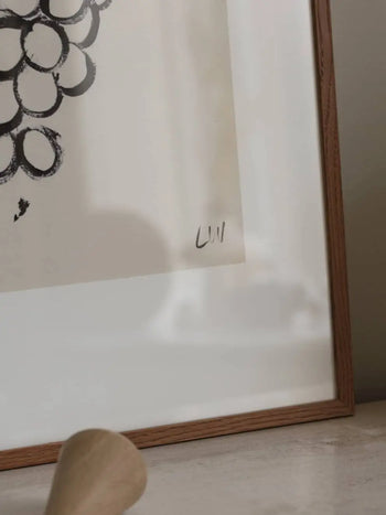 A close-up of The Poster Club Lena Wigers - Grapes (50x70), a framed abstract black and white giclée print with a minimalist wooden frame and Lena Wigers’ “Lill” signature on the border, available from The Poster Club.