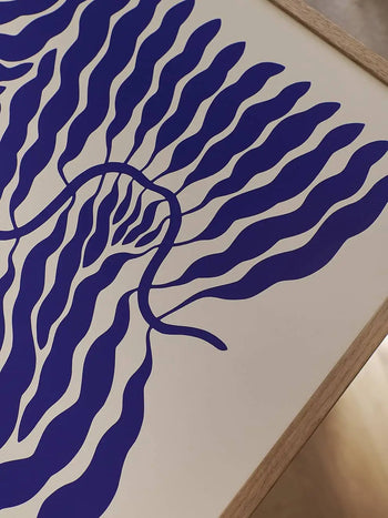 The Poster Club Linnéa Andersson - Little Blue (50x70) art print features wavy blue lines radiating from a central shape on a cream background, evoking stylized leaves or water. Framed in light wood, its inspired by Andersson’s signature leaf motif.