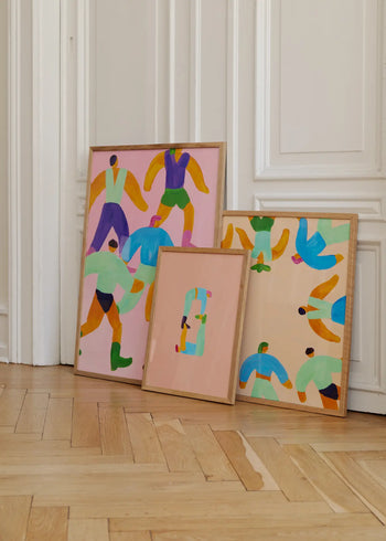 Three framed On The Edge giclée prints (30x40) by Danish artist Lise Uhrskov for The Poster Club sit on a light wooden floor, displaying stylized human figures in bright clothes against pink and beige backgrounds.