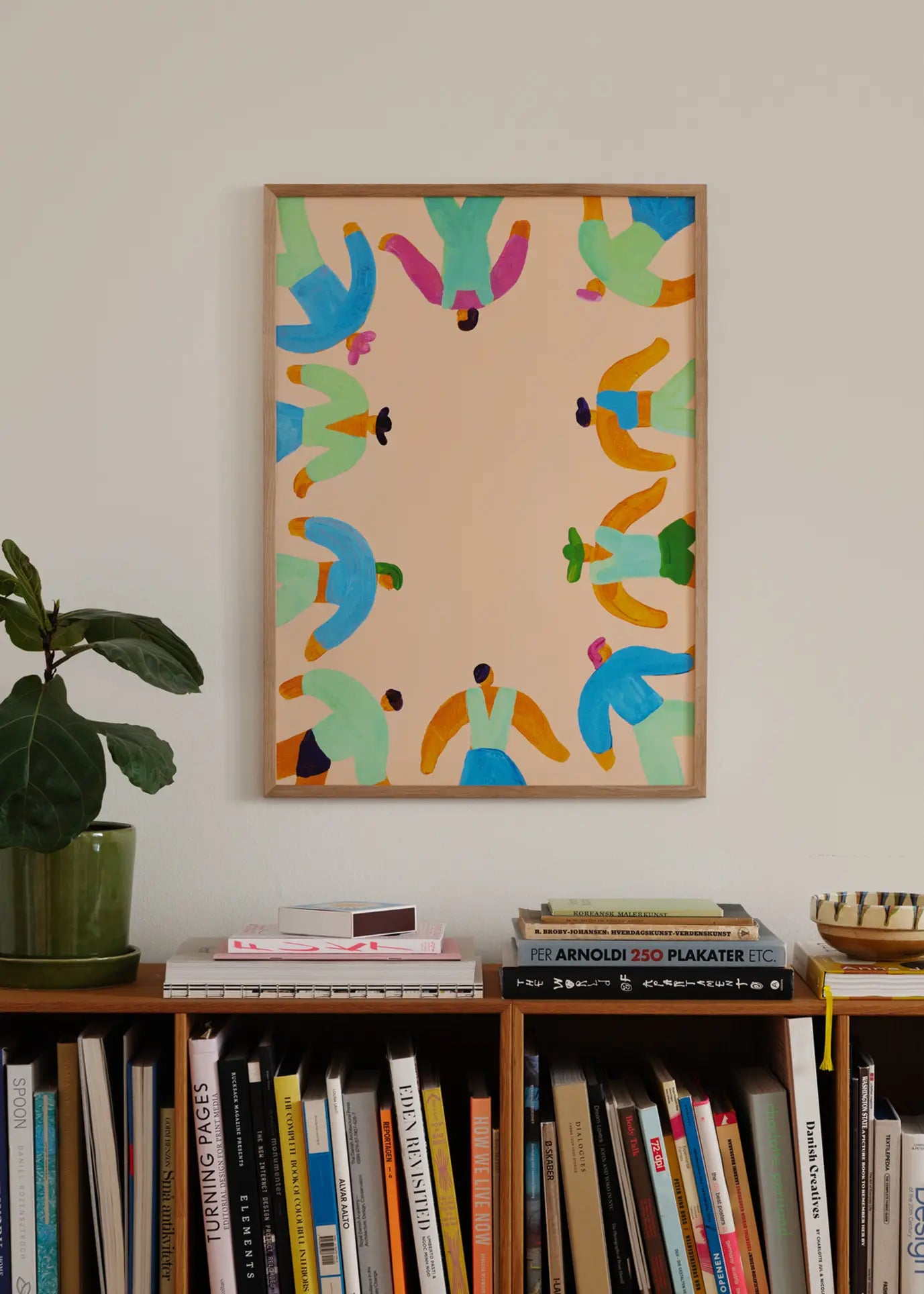 A framed The Poster Club Lise Uhrskov - On The Edge (30x40) print hangs above a bookshelf with books, magazines, a potted plant, and decor accents.