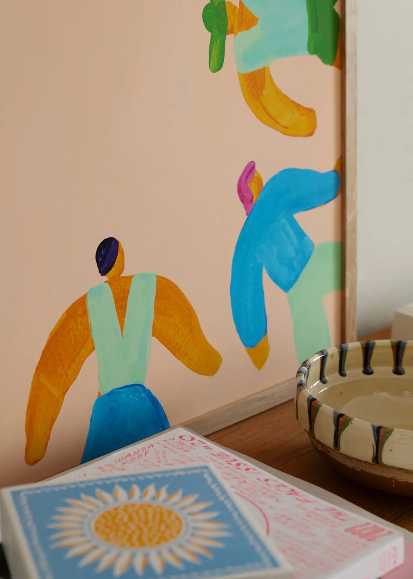 The Poster Club Lise Uhrskov - On The Edge (50x70) fine art giclée print on premium art paper features colorful abstract art, displayed above a wooden surface with a ceramic bowl and a sunflower-illustrated book.